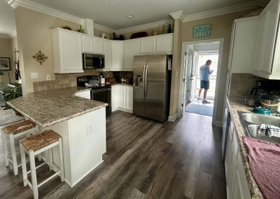 Bright kitchen with white cabinets, granite counters, and a person standing at the open door to the deck.
