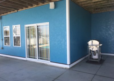 Blue stucco patio wall with sliding glass door, windows, and a stainless grill on a concrete floor.