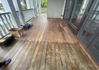 A wooden porch half-cleaned, showing a clear contrast between treated and untreated floorboards.