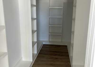 A walk-in closet with white shelves and wooden flooring, viewed from the doorway.