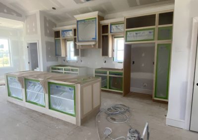 Kitchen under construction with cabinets and island covered in protective plastic and painter’s tape.