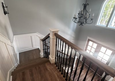 View from the top of a staircase with wood flooring, black railing, chandelier, and arched window.