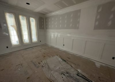 A room under renovation with unfinished walls, taped drywall, and a drop cloth on the floor.