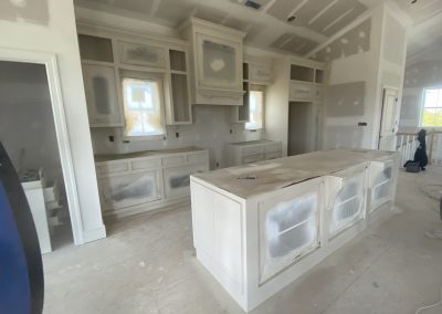 A kitchen under construction with unfinished cabinets, an island, and unpainted drywall.