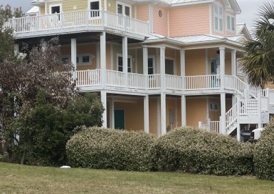 A large pastel peach and yellow beach house with white trim, wraparound porches, and a metal roof.