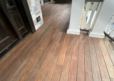 A wooden porch with a railing, leading to the entrance of a house with stone and brick walls.