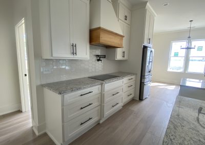 Modern kitchen with white cabinets, granite countertops, wood range hood, and light wood floors.