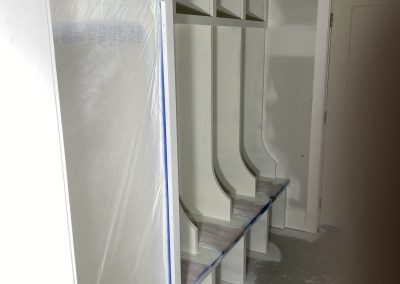 Built-in cubbies and bench in a mudroom, partially painted with protective plastic covering some surfaces.