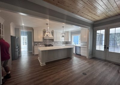 Bright kitchen with white cabinets, island, wood floor, and ceiling; man in red shirt stands on the left.