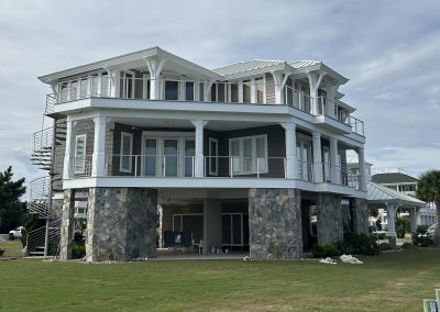 A modern two-story beach house with stone pillars, wraparound balconies, and large windows.