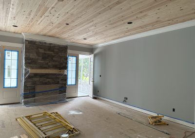 A room under renovation with a wood ceiling, gray walls, and covered fireplace; tools on the floor.