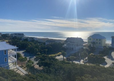 View of houses by the ocean with sunlight reflecting on the water and a clear blue sky overhead.
