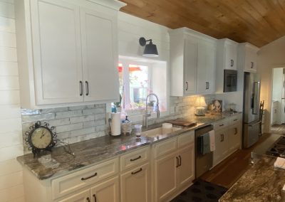 Modern kitchen with white cabinets, granite countertops, and a wood-paneled ceiling, featuring a window above the sink.