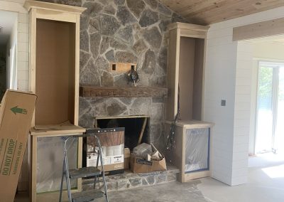 Stone fireplace with wooden mantel, unfinished built-ins, boxes, and a step stool in a room under renovation.
