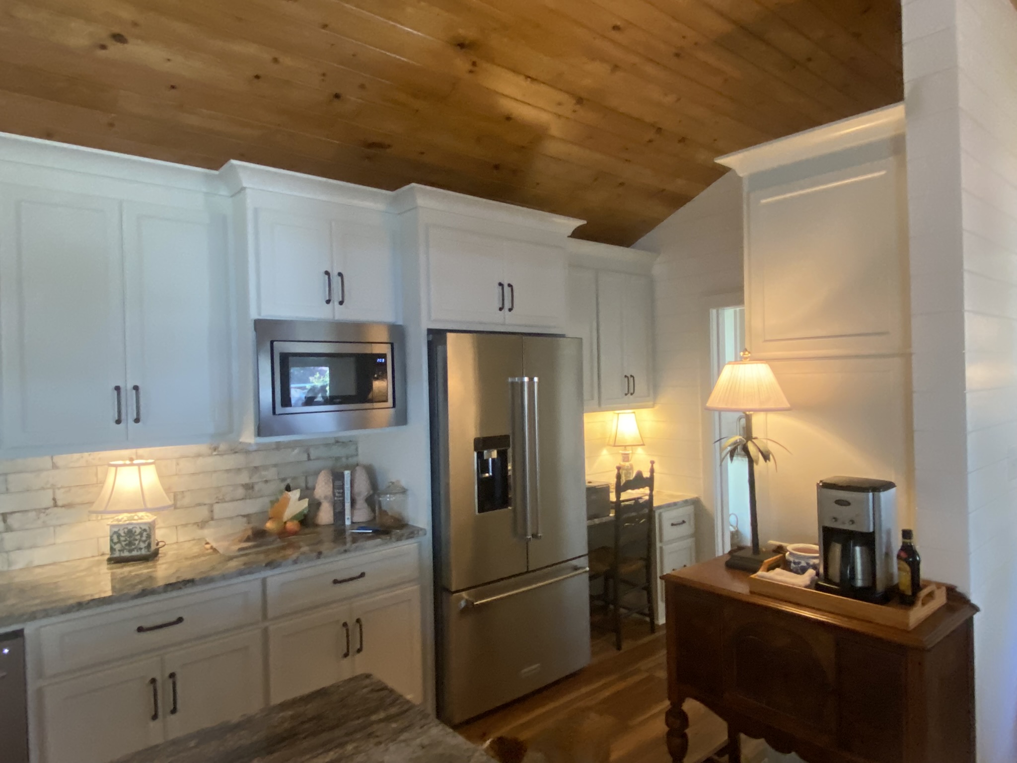 C8030584-18F0-47C2-AE22-E457E448B9B5_1_102_o A cozy kitchen with white cabinets, a stainless fridge, and warm lighting from two table lamps.