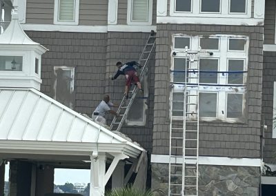 Two men on ladders work on the exterior wall of a multi-story house under renovation.
