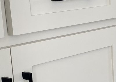 Close-up of white kitchen cabinets and drawers with modern black handles.