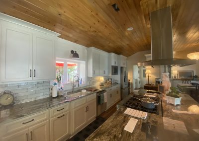 A modern kitchen with white cabinets, granite countertops, and a wooden ceiling, viewed in natural light.