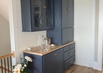 Blue built-in cabinets with a wood countertop, glassware, flowers in a vase, and a dog on a hardwood floor.