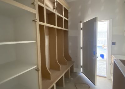 Tall wooden shelves and cubbies in a room under construction with an open door and extension cord on the floor.