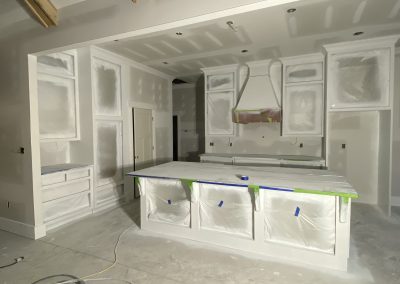 A kitchen under construction with cabinets and island covered in protective plastic and tape.