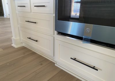 White kitchen cabinets and drawers with black handles next to a stainless steel oven with protective blue tape.