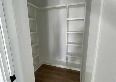 Empty white walk-in closet with built-in shelves and wooden floor.