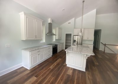 Modern kitchen with white cabinets, marble countertops, stainless steel appliances, and wood flooring.