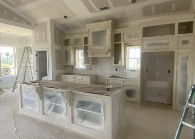 A kitchen under renovation with plastic-covered cabinets, ladders, and unfinished drywall.