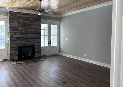 Living room with wood ceiling, stone fireplace, gray walls, and dark wood floor, with doors to outside.