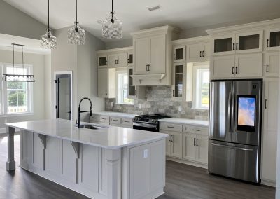 Modern kitchen with white cabinets, marble island, stainless steel appliances, and pendant lights.