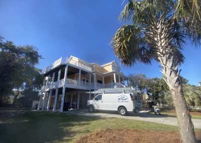 A large beach house with balconies and a white van parked in the driveway under a clear blue sky.