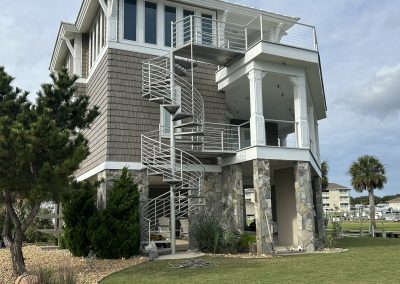 Modern two-story house with a spiral staircase, stone pillars, and landscaped lawn under a partly cloudy sky.