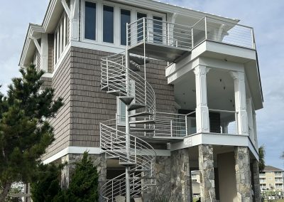 Three-story house with stone base and a metal spiral staircase leading to upper balconies.
