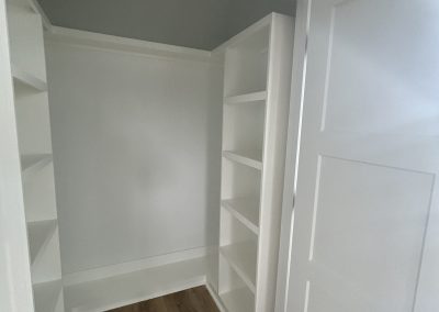 A small, empty white closet with built-in shelves and wooden floor, door partially open.