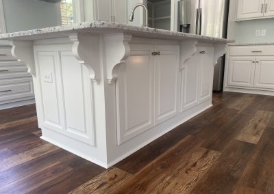 White kitchen island with decorative corbels and marble countertop on dark wood flooring.