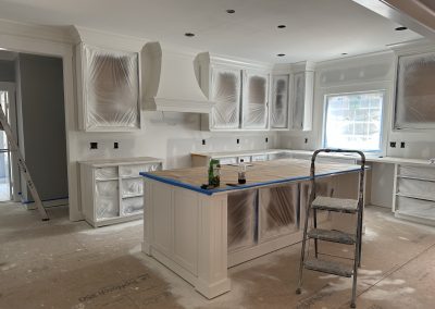 A kitchen under renovation with cabinets covered in plastic, a ladder, and tools on the island.