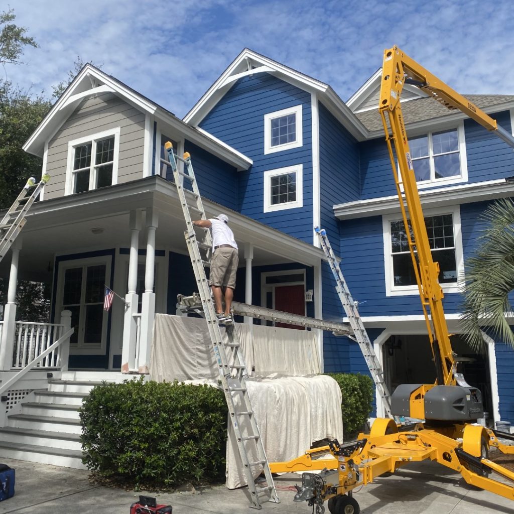 IMG_1520-Jackson-Salterpath-1024x1024-1 Residential Painting: A man on a ladder repairs a two-story blue house, with another ladder and yellow lift nearby.